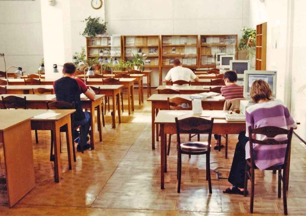 Biblioteka, ul. Parkowa, czytelnia studencka, rzędy stolików z krzesłami, przy których siedzą czytelnicy. Z prawej strony na każdym stole stoi komputer. Na końcu pomieszczenia i po prawej stronie pod ścianą regały z książkami.