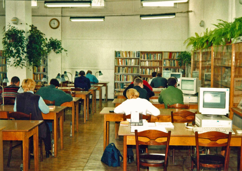 Biblioteka, ul. Parkowa, czytelnia studencka, rzędy stolików z krzesłami, przy których siedzą czytelnicy. Z prawej strony na każdym stole stoi komputer. Na końcu pomieszczenia i po prawej stronie pod ścianą regały z książkami.